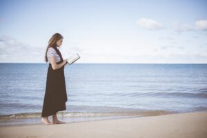 Morning Prayer For Widows: Woman walking along the beach at sunrise with footprints in the sand