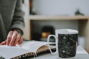 A person reading the Bible beside a steaming cup of coffee at sunrise