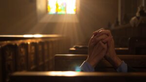 Early morning light shining through a church window, with hands clasped in prayer